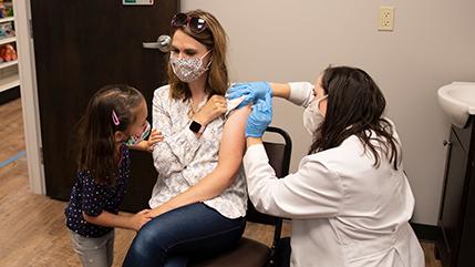Pharmacist vaccinating a patient with little girl looking on
