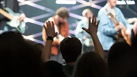 Student raising h和s to praise God during chapel service
